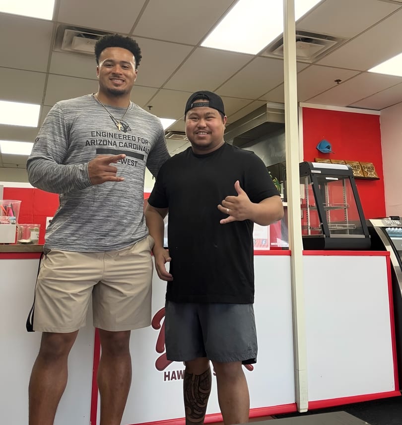 Two men, one tall in a gray shirt and one shorter in a black shirt, pose in a restaurant.